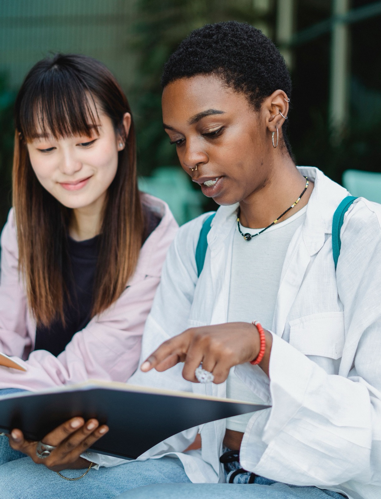 Two young women talking together outdoors with study materials