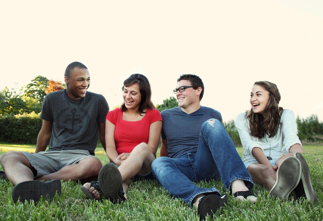 Four young people smiling and chatting while sitting on the grass