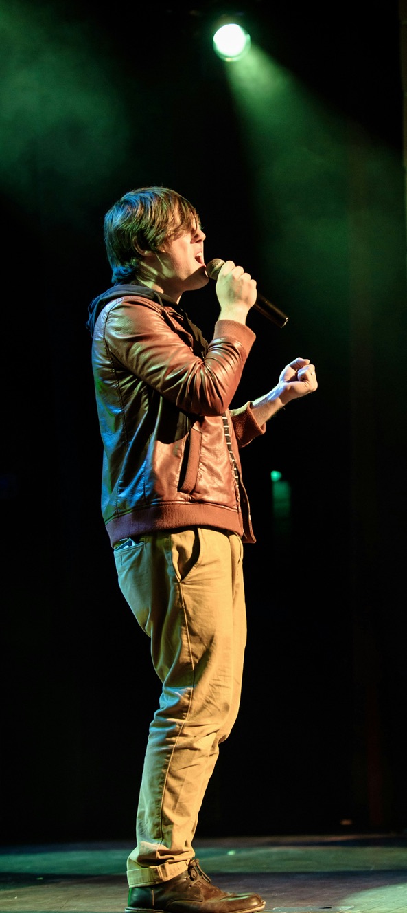 A singer performing with a handheld microphone under green stage lights